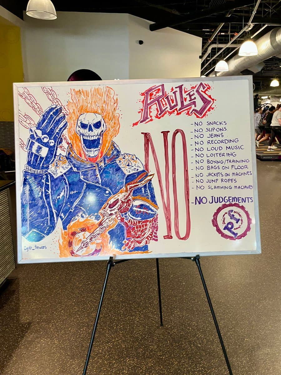 A whiteboard on an easel in a gym displays a colorful, hand-drawn illustration of the character Ghost from Call of Duty alongside a list of gym rules. The board is titled 'RULES' and features a large 'NO' next to the list of prohibited items.