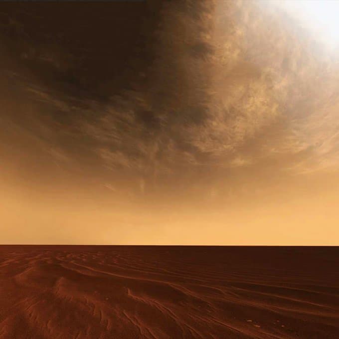 A panoramic view of the Martian surface showing a flat, reddish-brown landscape under a hazy, orange sky with wispy clouds. The image captures a cloudy day on Mars as seen by the Curiosity rover.
