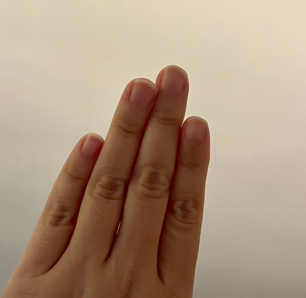 A close-up photograph of a person's hand held up against a plain, light-colored background, showing the fingers and nails. The image illustrates the concept of finger length and digit ratio mentioned in the accompanying text.