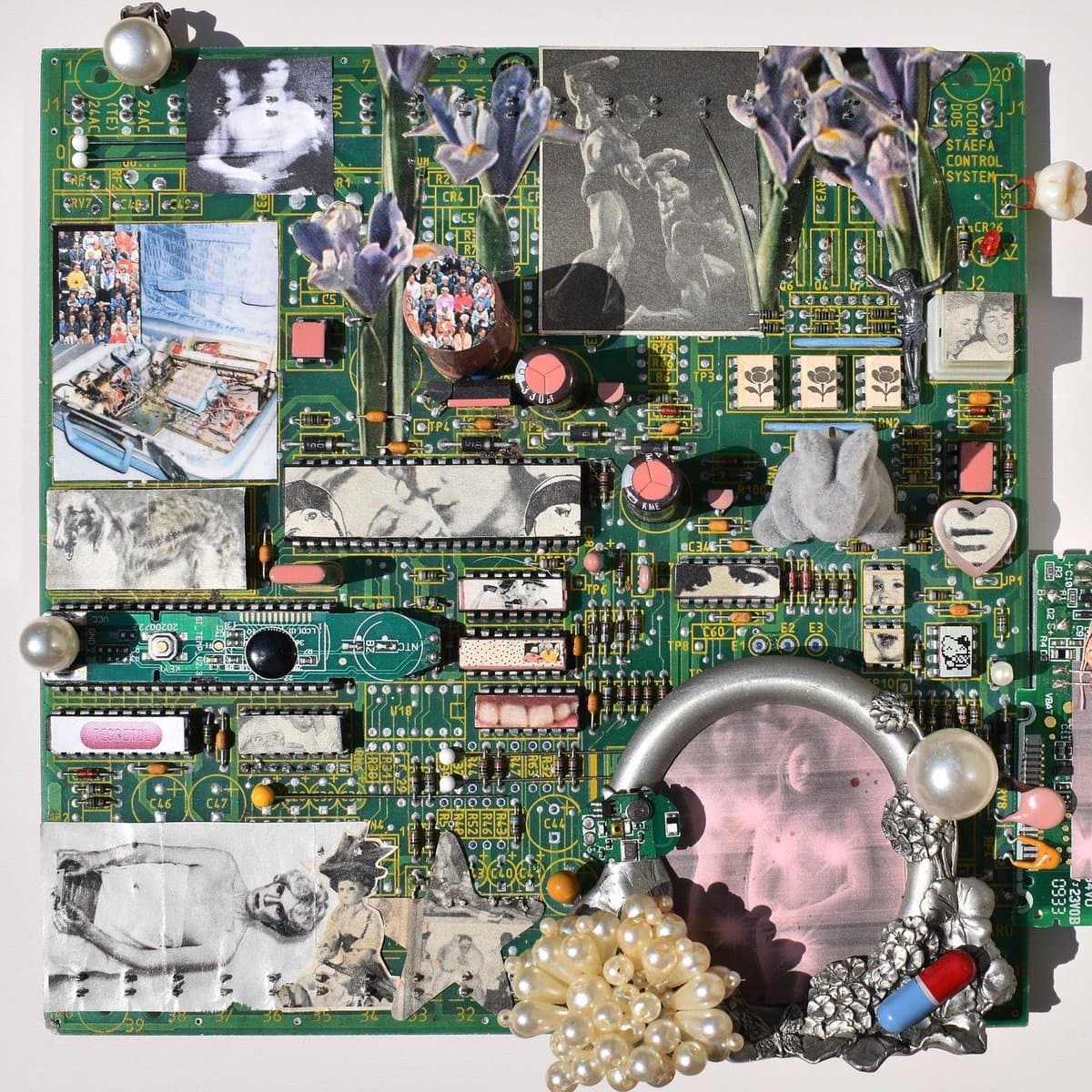 A mixed-media art piece created on a green printed circuit board, featuring embedded black-and-white photographs, purple flowers, pearls, a large ring, and various electronic components. The board is labeled 'STAEFA CONTROL SYSTEM' in the upper right corner.