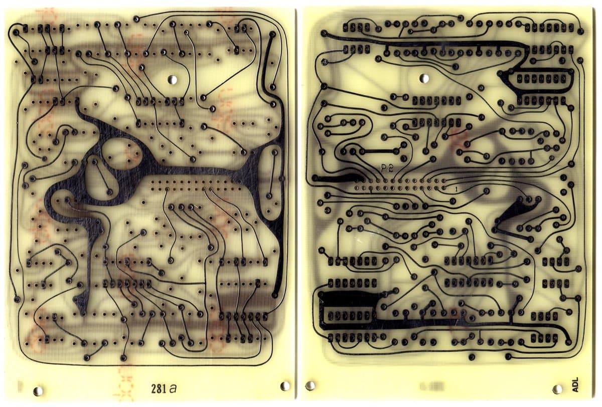 A photograph showing the two sides of a vintage printed circuit board (PCB) with intricate black copper traces and solder pads on a yellowish substrate. The left side is labeled '281a' and the right side is labeled 'ADL' at the bottom.