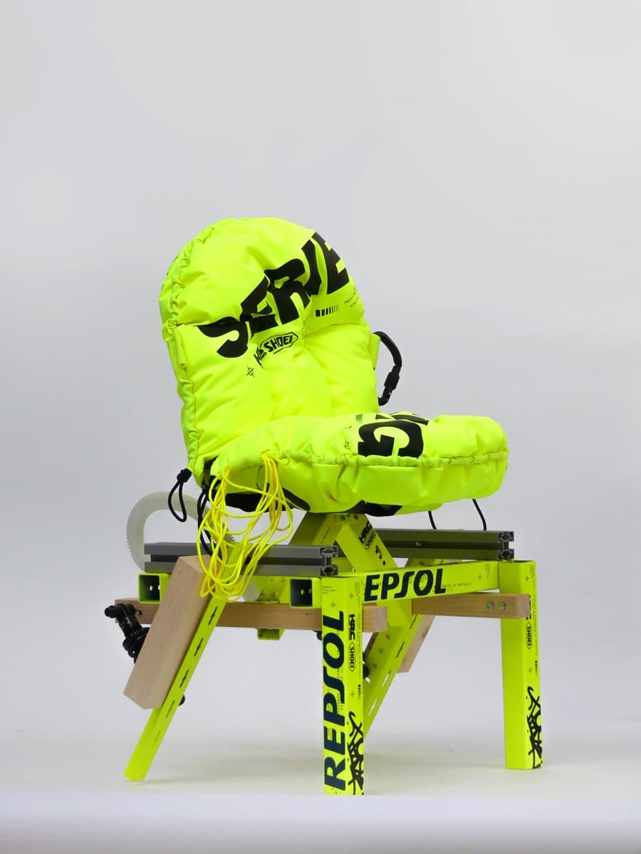 A studio photograph of a bright neon-yellow, puffy chair with black graphic text, mounted on a matching yellow and wooden frame structure.