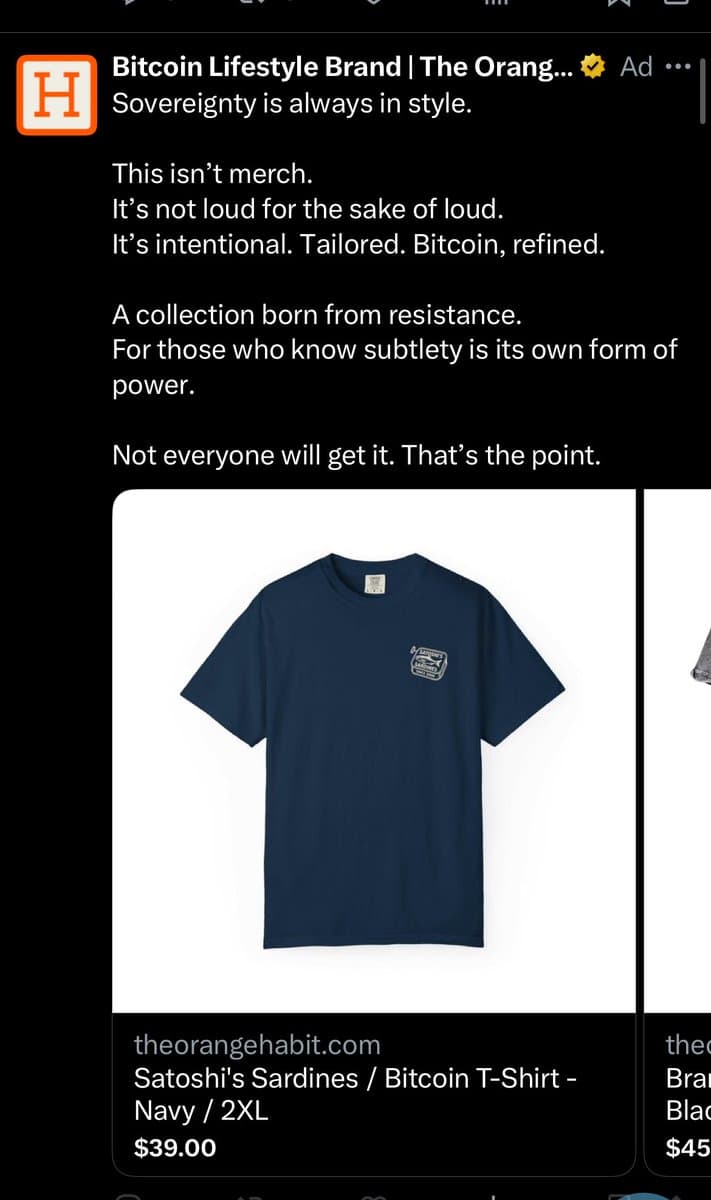A screenshot of a Twitter advertisement for a Bitcoin lifestyle brand called 'The Orange Habit.' The ad features a dark blue t-shirt with a small logo and includes text describing the collection as intentional and tailored for those who value subtlety.