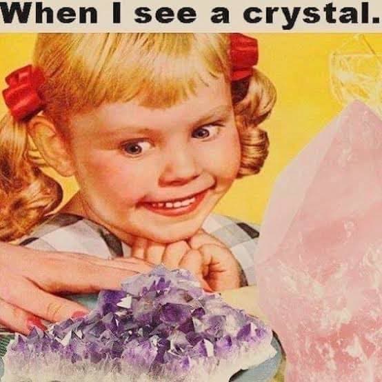 A meme featuring a vintage photograph of a young girl with red hair bows smiling excitedly at a cluster of purple amethyst crystals and a large pink crystal. The image is overlaid with text at the top.