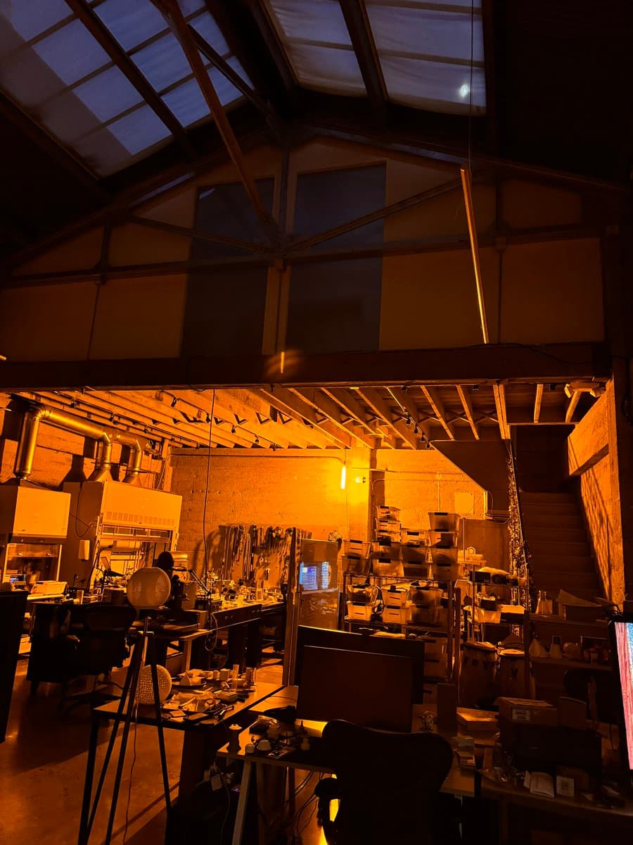 A wide-angle photograph of a dimly lit laboratory interior at night, featuring workbenches, scientific equipment, and a high, slanted ceiling with skylights.