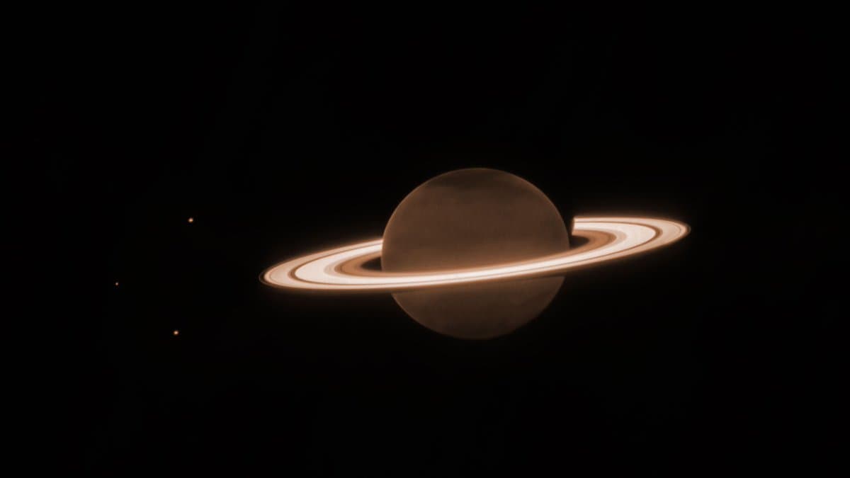 A digital rendering of a ringed gas giant planet, resembling Saturn, set against a black background with a few distant stars. The planet is illuminated from the side, highlighting its spherical shape and the distinct bands of its rings.